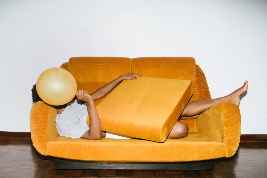 person lying on sofa with face hiding behind a balloon